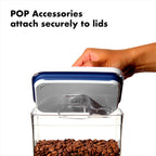 Hand holding a blue lid on a container with coffee beans, text 'POP Accessories attach securely to lids'.