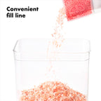 Pink Himalayan salt being poured into a clear container with text 'Convenient fill line'.